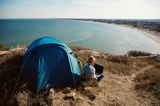 Happy woman sitting near tent with laptop