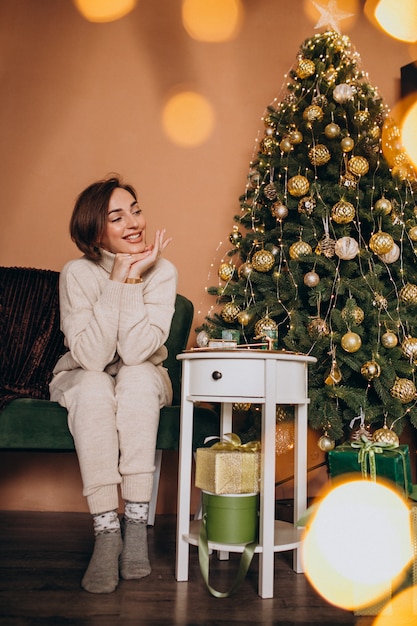 Free photo happy woman sitting on sofa by the christmas tree