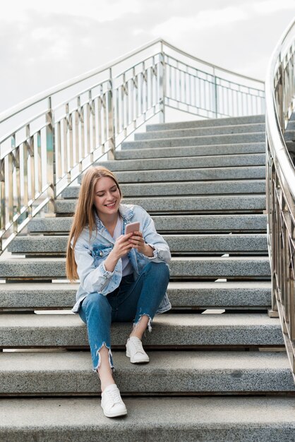 Happy woman sitting on staircases and using smartphone