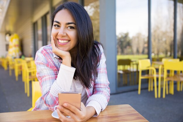 Happy woman sitting in street cafe with smartphone and coffee