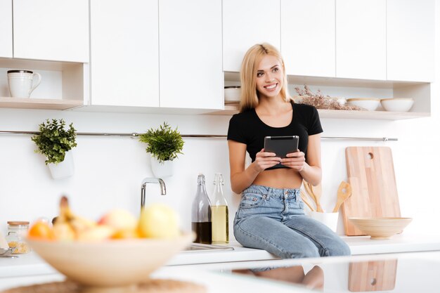 Happy woman sitting on table and holding tablet