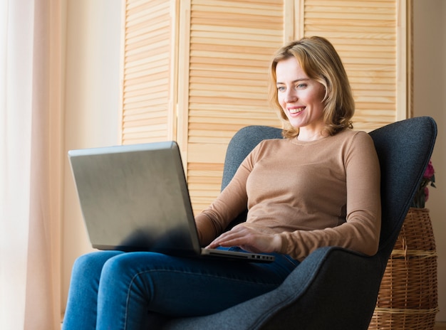 Счастливая женщина сидит и с помощью ноутбука