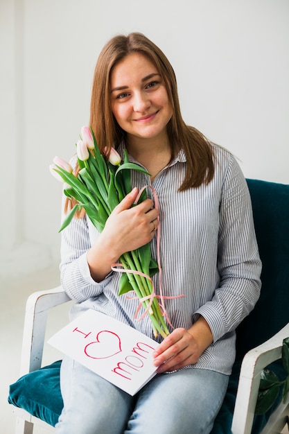 Happy woman sitting with greeting card and flowers