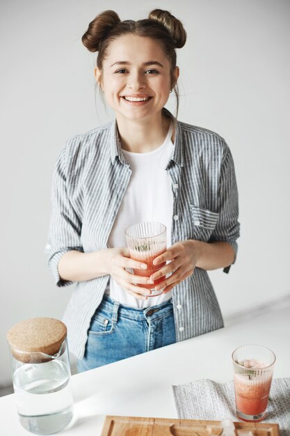 Happy woman smiling holding glass with grapefruit detox smoothie over white wall. Healthy diet food.