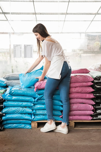 Happy woman stacking plastic sacks in greenhouse