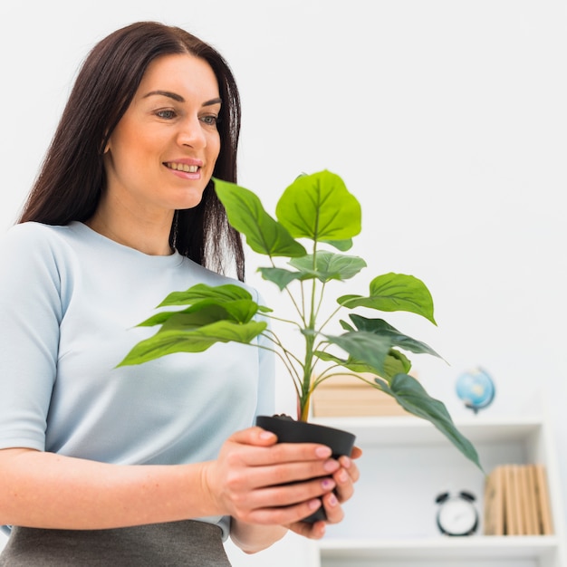 Foto gratuita donna felice che sta con la pianta verde in vaso di fiore