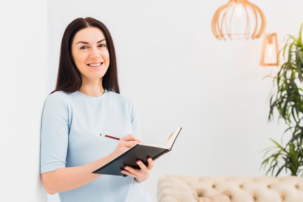 Free photo happy woman standing and writing in notebook