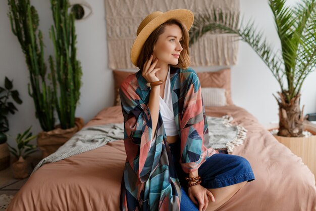 Happy woman in straw hat siting in bohemian bedroom