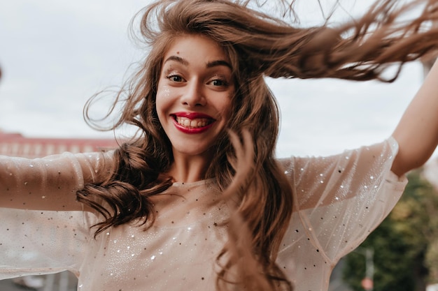 Free photo happy woman in stylish outfit smiles widely and poses on balcony cheerful girl in white dress with sparkles takes selfie