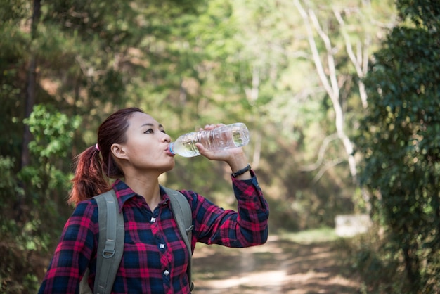 自然の中でリュックサックの飲み水を持つ幸せな女性の観光客。