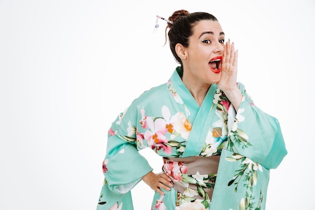 Donna felice in kimono giapponese tradizionale che grida o chiama qualcuno che tiene la mano vicino alla bocca su bianco