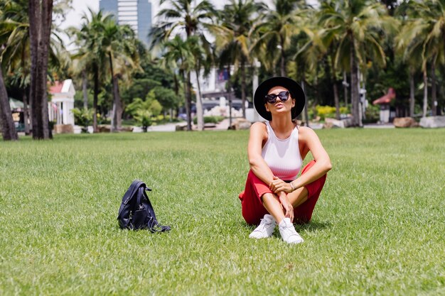Счастливая женщина путешествует по Бангкоку с рюкзаком, наслаждаясь прекрасным солнечным днем в тропическом парке на поле зеленой травы