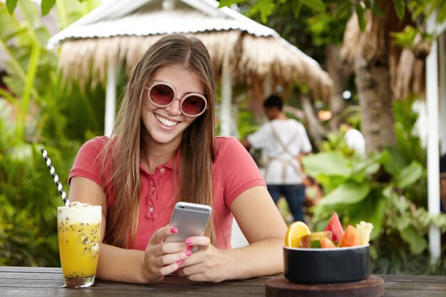 Счастливая женщина, использующая бесплатный Wi-Fi на своем мобильном телефоне, смотрит на экран с радостной флиртующей улыбкой