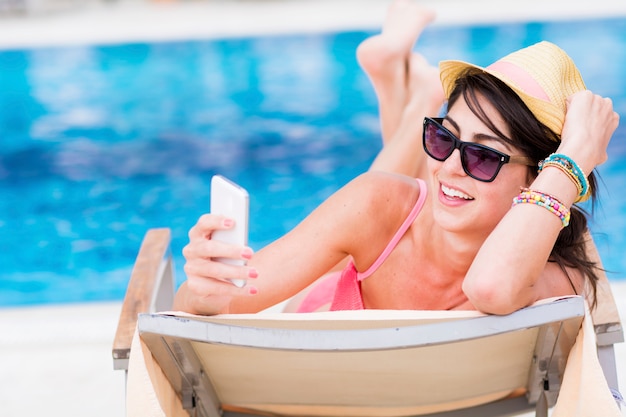 Happy woman using her mobile on the deck chair