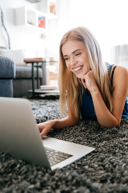 床のカーペットの上にラップトップコンピューターを使用して幸せな女