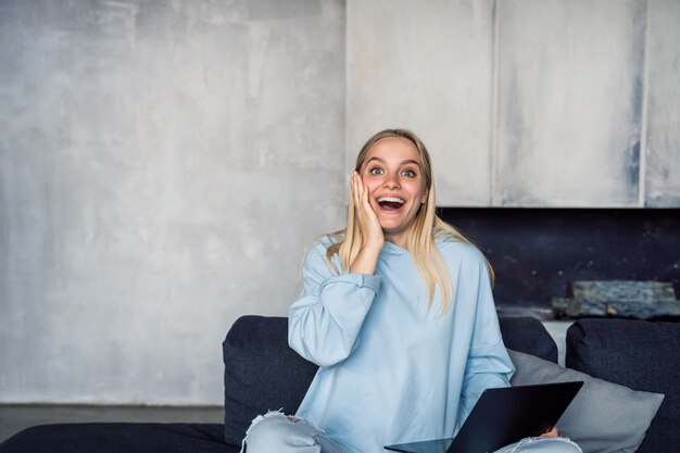 Happy woman using silver laptop while sitting on sofa