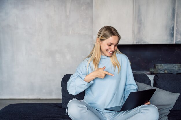 Happy woman using silver laptop while sitting on sofa