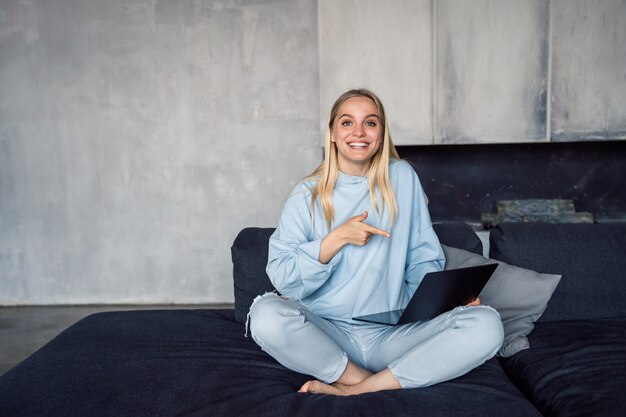 Happy woman using silver laptop while sitting on sofa