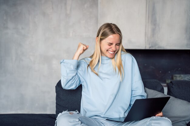 Happy woman using silver laptop while sitting on sofa