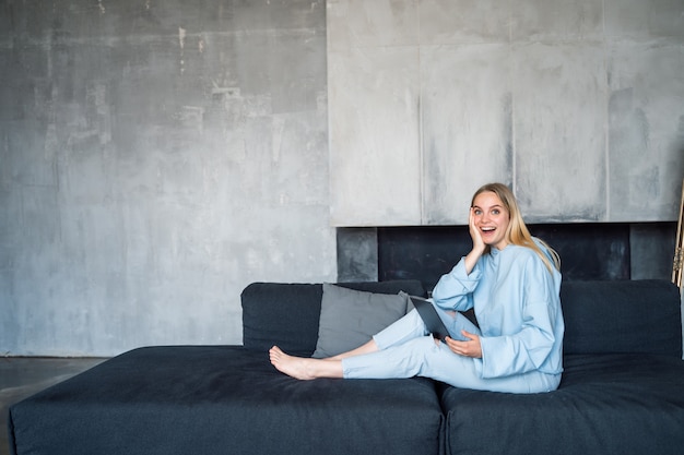 Happy woman using silver laptop while sitting on sofa