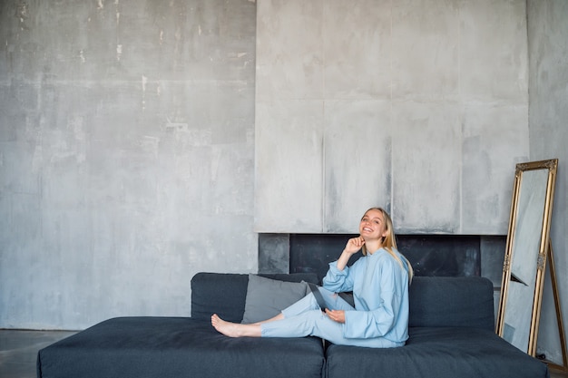 Happy woman using silver laptop while sitting on sofa