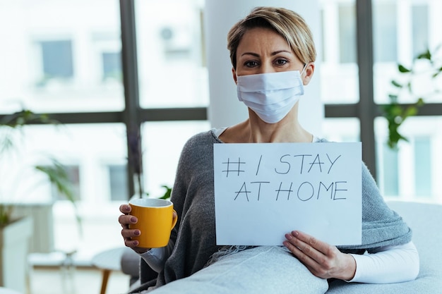 Free photo happy woman wearing face mask and holding placard with hashtag i stay at home