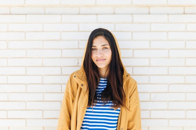 Happy woman wearing jacket standing against brick wall