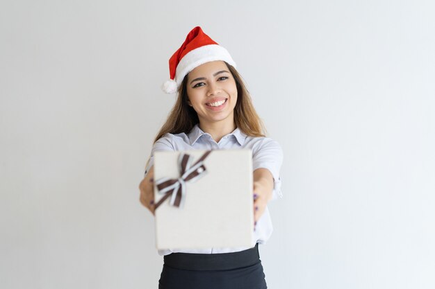 Happy woman wearing Santa Claus hat and giving gift box