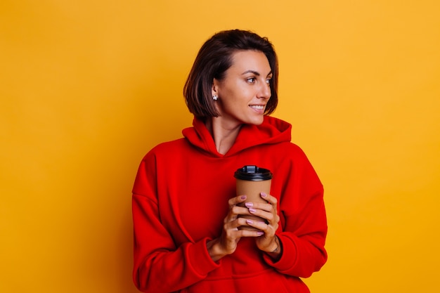 Happy woman wearing warm winter clothes warms herself with cup of hot coffee