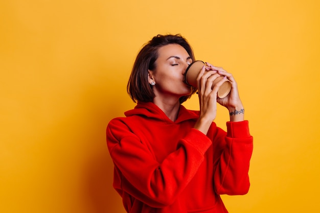 Happy woman wearing warm winter clothes warms herself with cup of hot coffee