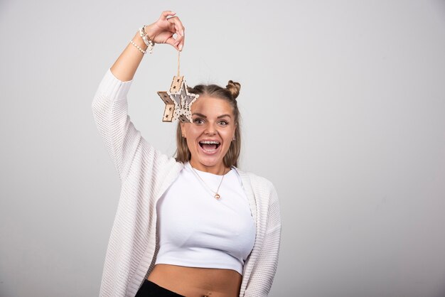 Happy woman in white outfit holding wooden star on gray background.