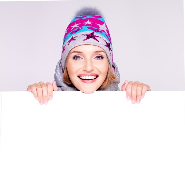 Happy woman in winter outerwear over white placard in hands