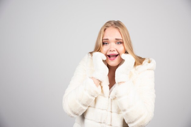 Happy woman in winter outfit posing on gray wall.