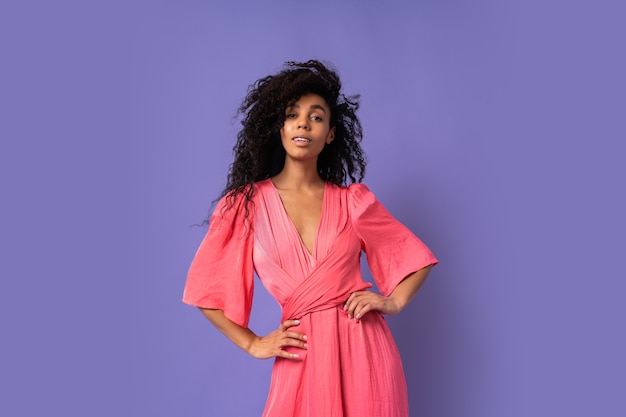 Free photo happy woman with  curly hairs posing in stydio over purple wall. wearing elegant party dress. spring fashion look.