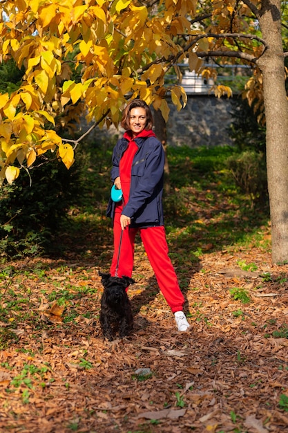 Happy woman with dog in park with autumnal leaves