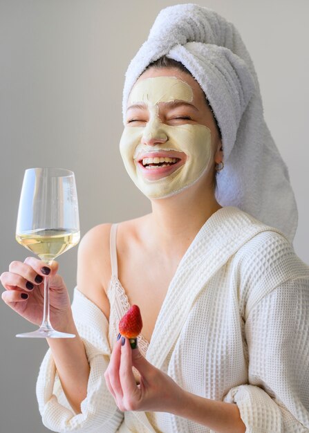 Happy woman with face mask holding glass of wine and strawberry