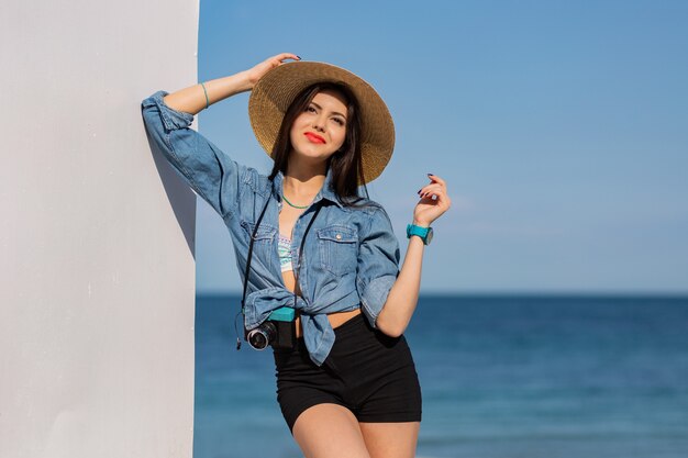 Happy woman with figure in shorts and straw hat posing on the beach.