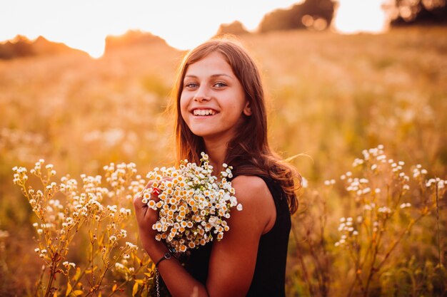 花の幸せな女性は、夕方のフィールドに立っている