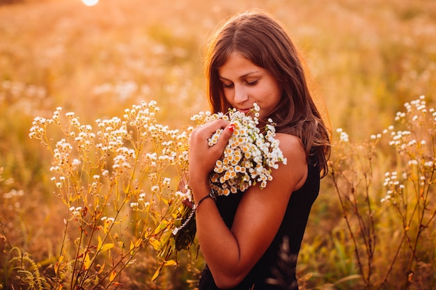 Foto gratuita la donna felice con i fiori si leva in piedi sul campo di sera