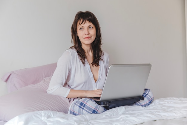 Happy woman with laptop on bed