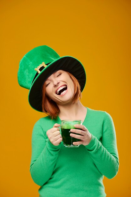 Бесплатное фото Счастливая женщина в шляпе лепрекона пьет пиво