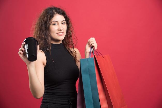 Happy woman with many of bags and cup on red