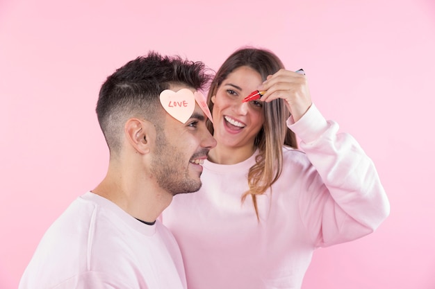 Free photo happy woman with marker near young man with paper hearts on front