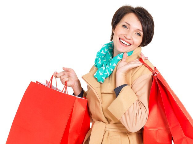 Happy woman with shopping bags in beige autumn coat with green scarf isolated on white