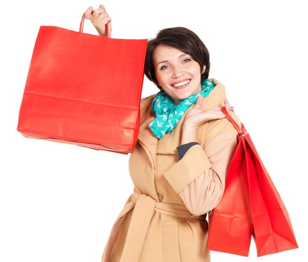 Happy woman with shopping bags in beige autumn coat with green scarf isolated on white