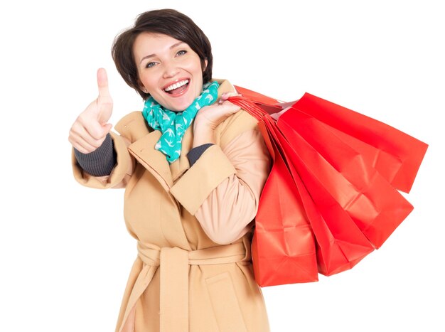 Happy woman with shopping bags in beige autumn coat with green scarf isolated on white