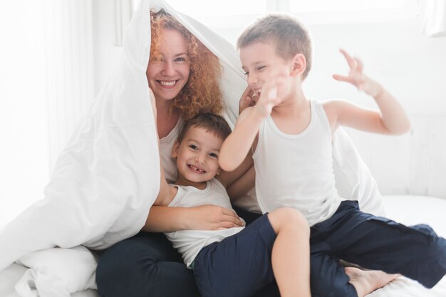 Счастливая женщина, завернутая в одеяло, играющая с сыновьями