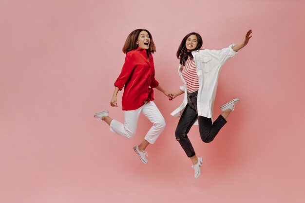 Happy women jump on isolated background Tanned Asian girls in stylish outfits move on pink backdrop