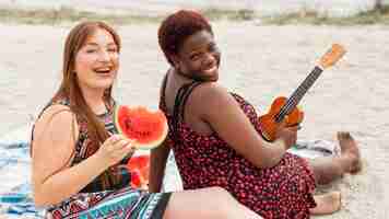 Free photo happy women posing at the beach with watermelon and guitar