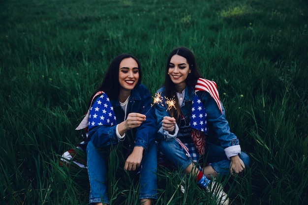 Free photo happy women sitting on grass with bengal lights